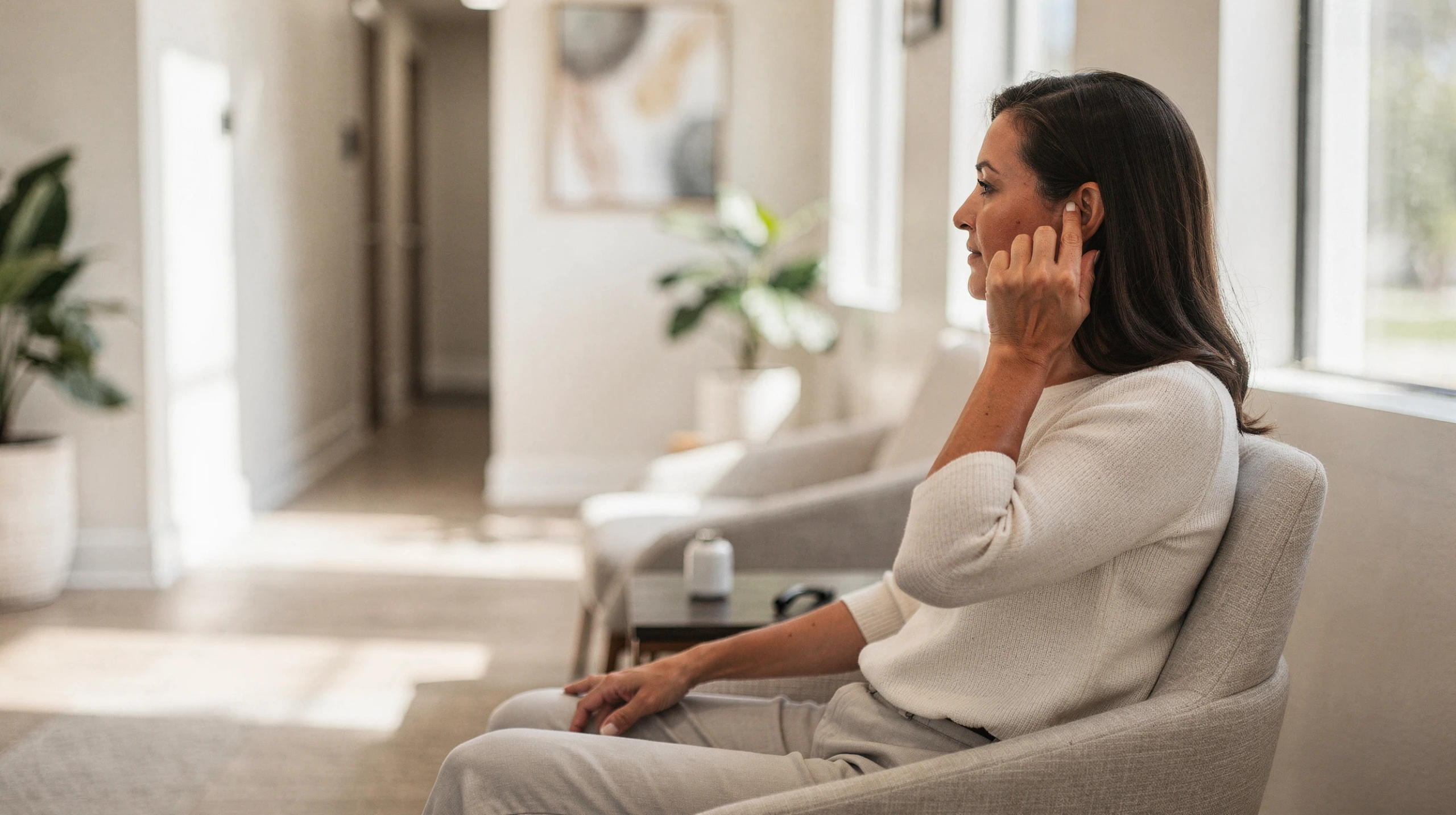 Woman sitting in a bright clinic waiting area, touching her face in discomfort